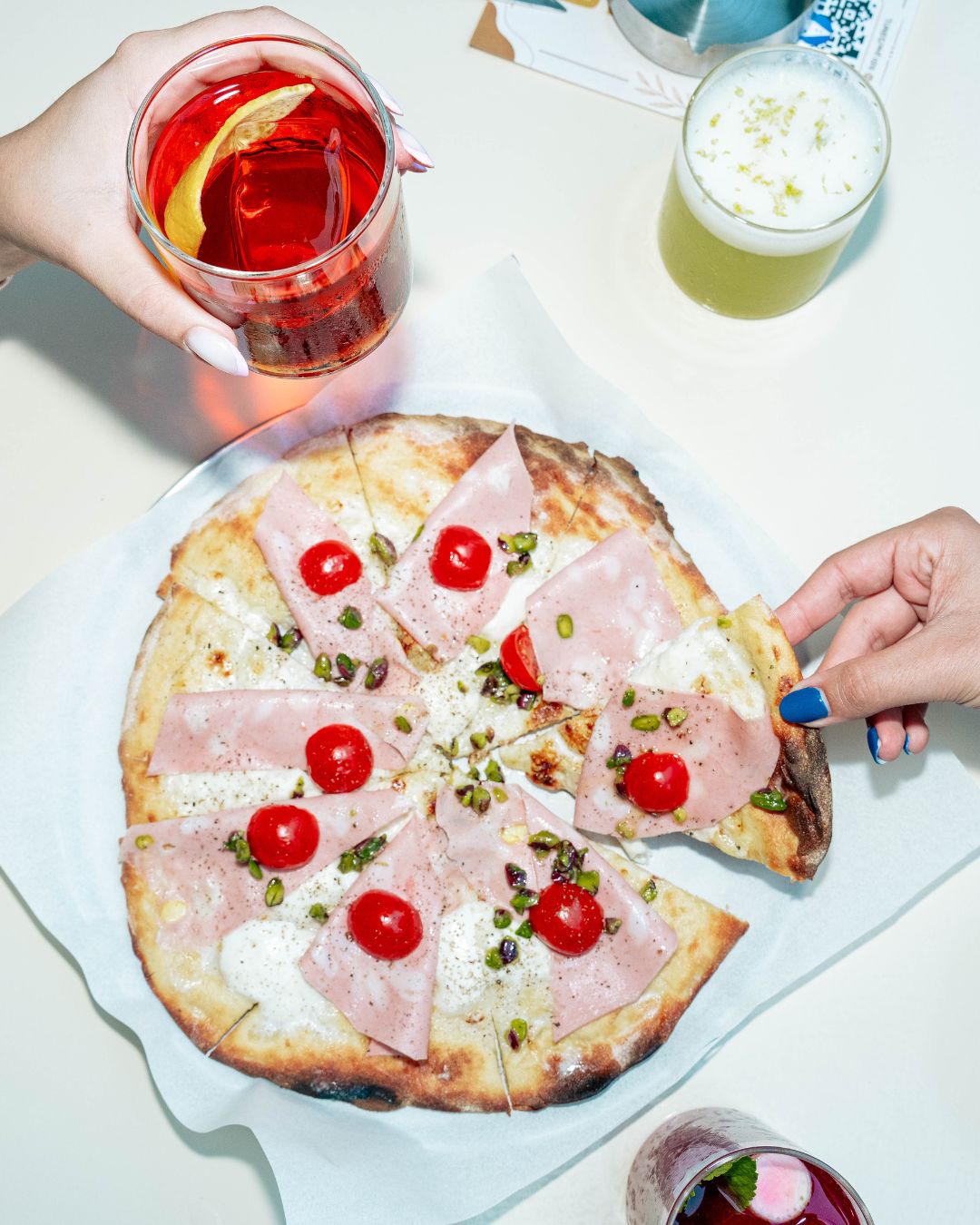 A mortadella and pistachio pizza served with colourful cocktails