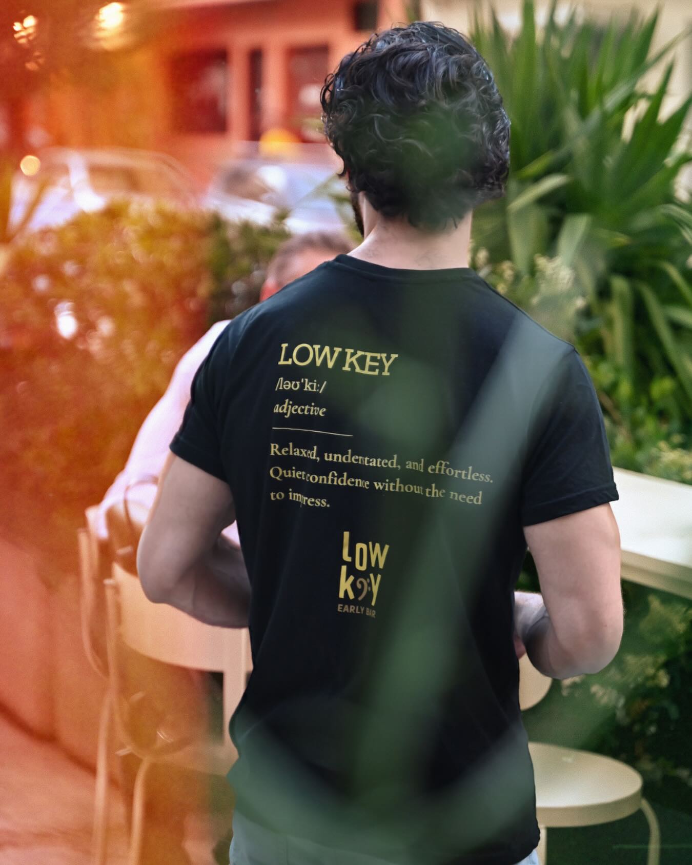 A guest wearing a Lowkey Early Bar t-shirt outside the bar in the evening
