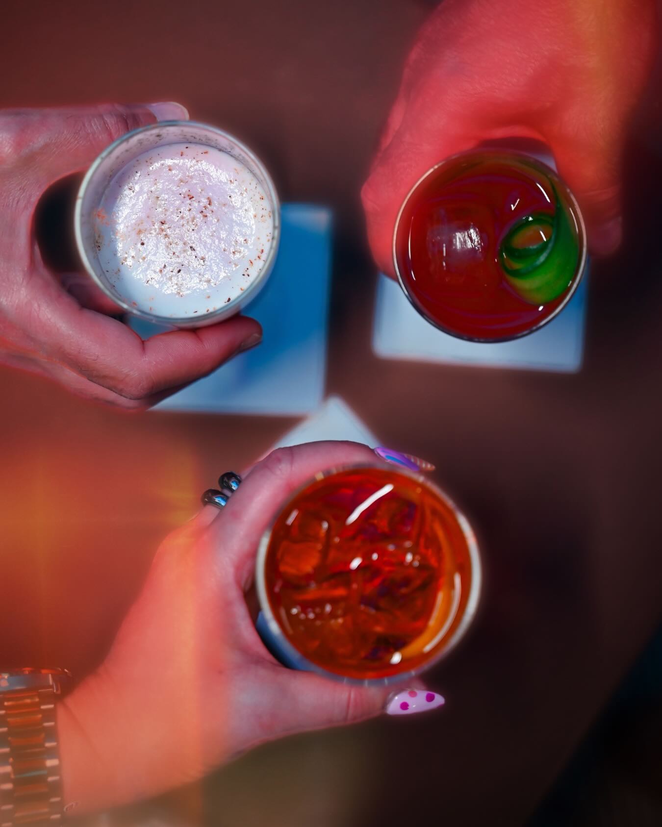 Three hands holding beautifully made cocktails from above